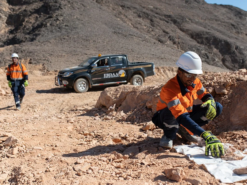 EBDAA geologist sampling rock at a surface outcrop beside a field truck